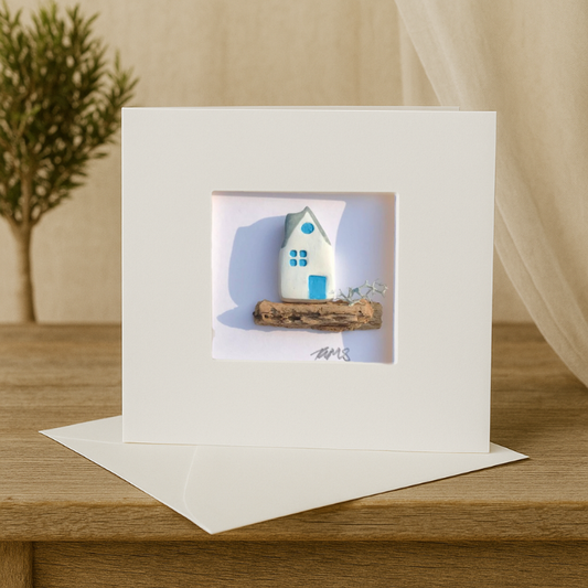 handcrafted coastal cottage art card with white and blue house on natural driftwood.