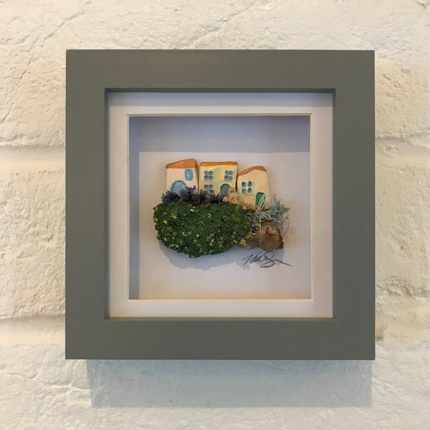 Framed 'Little Worlds' artwork featuring handcrafted clay houses with miniature gardens, set on driftwood and enclosed in a box frame.