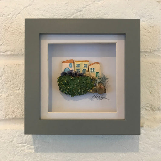 Framed 'Little Worlds' artwork featuring handcrafted clay houses with miniature gardens, set on driftwood and enclosed in a box frame.
