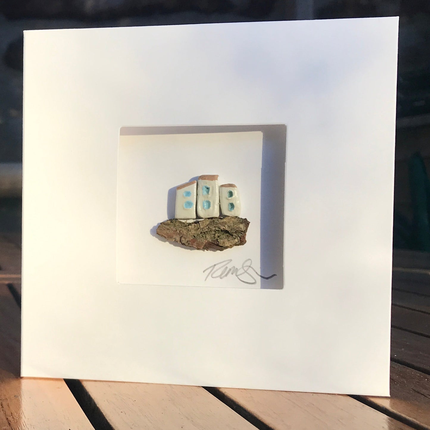 Little Hamlet card featuring three handcrafted clay houses on driftwood, framed in a 13.5 cm square aperture card