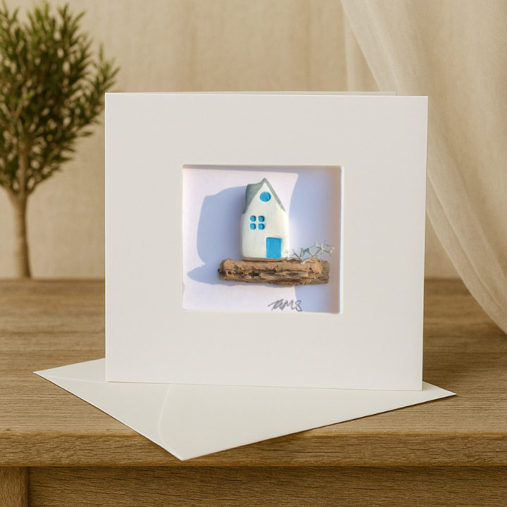 handcrafted coastal cottage art card with white and blue house on natural driftwood.