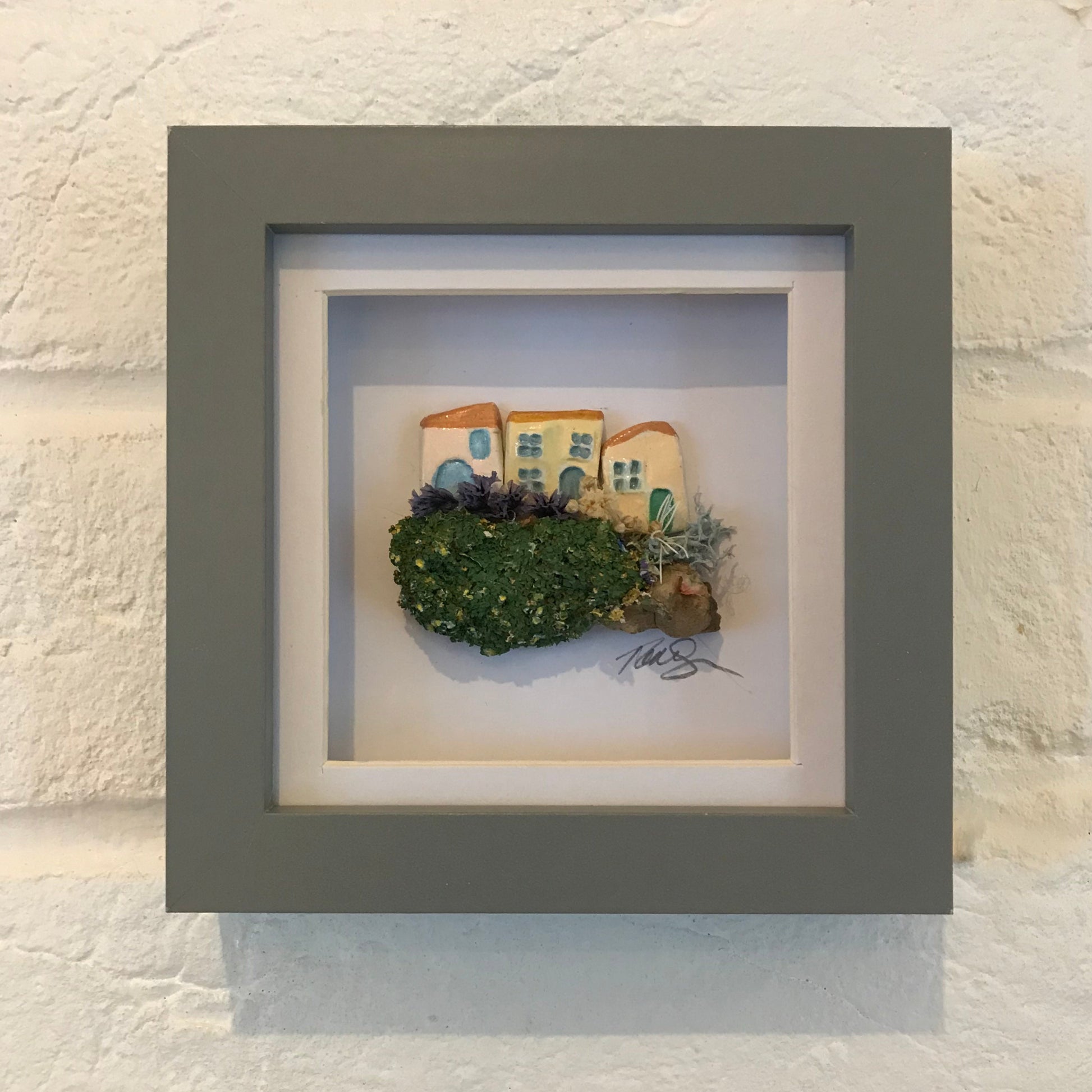 Framed 'Little Worlds' artwork featuring handcrafted clay houses with miniature gardens, set on driftwood and enclosed in a box frame.